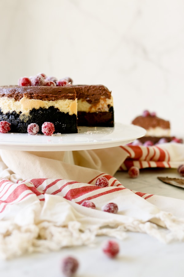 Triple Chocolate Layered Cheesecake on a white cake pedestal, garnished with sugared cranberries