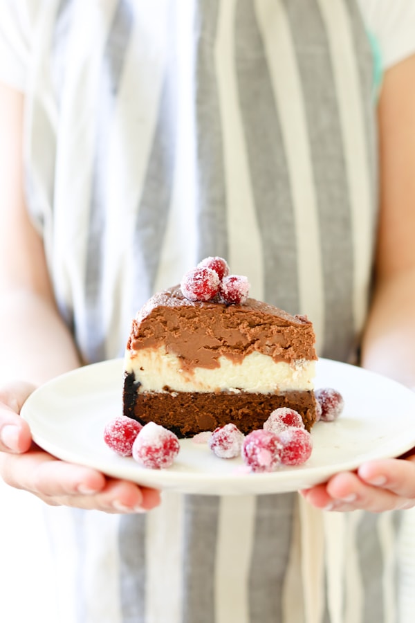 woman wearing a gray and white pin striped apron holding a white plate with Triple Chocolate Layered Cheesecake