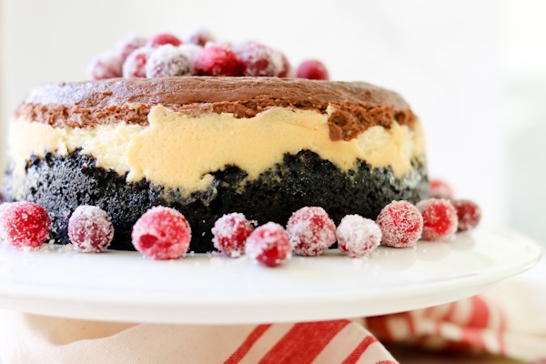 Pressure Cooker Triple Chocolate Layered Cheesecake on a white cake stand, garnished with sugared cranberries