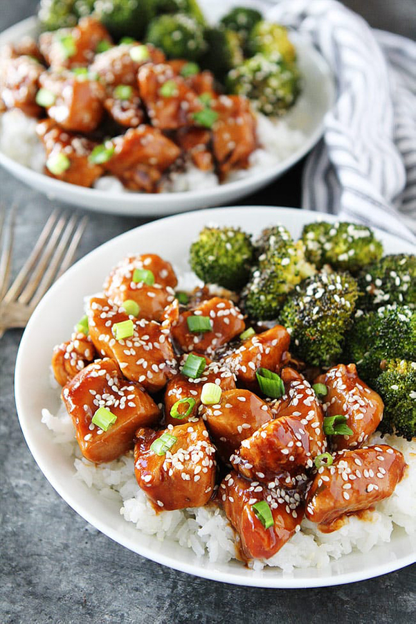45 degree shot of Instant Pot Sesame Chicken from Two Peas and Their Pod's review of the Electric Pressure Cooker Cookbook - featuring a white plate topped with white rice, brocccoli on half of the rice, and red sesame chicken garnished with sesame seeds and green onions on the other half