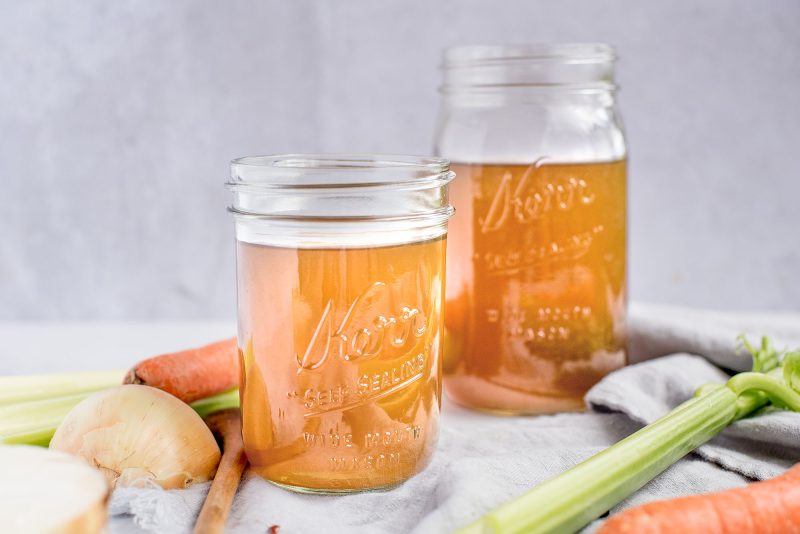 Two mason jars of vegetable stock made in the Instant Pot with celery and carrots on a gray napkin in the foreground