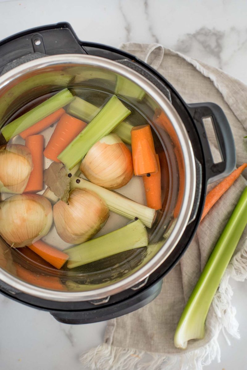 an overhead shot looking into an Instant Pot filled with rough chopped carrots, celery and quartered onions with skins on