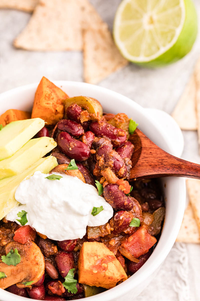 An overhead shot of a wooden spoon scooping up a bite of vegetarian chili with diced avocados and sour cream as garnish