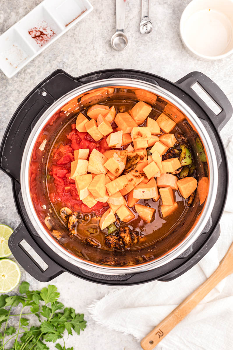 An overhead shot looking into the pressure cooker cooking pot, adding the sweet potatoes, spices, and broth to the vegetarian chili