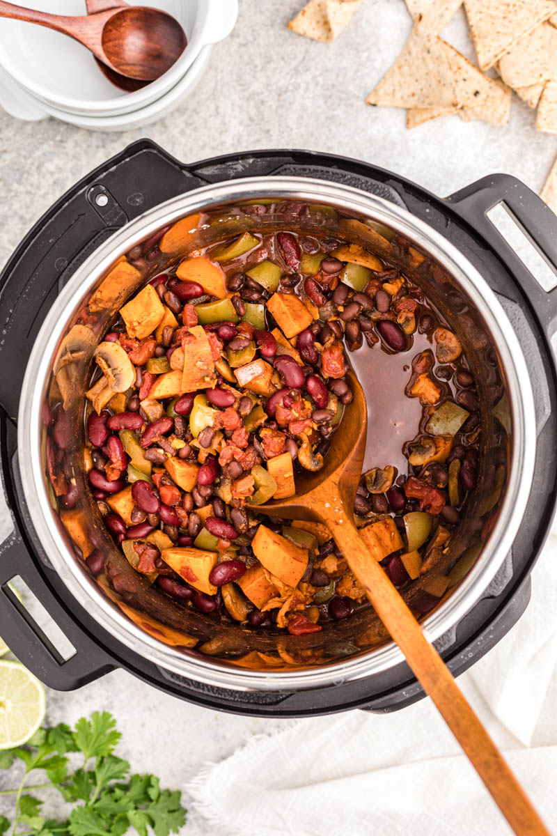 An overhead shot looking into the Instant Pot with a wooden spoon showing the chili before it thickens