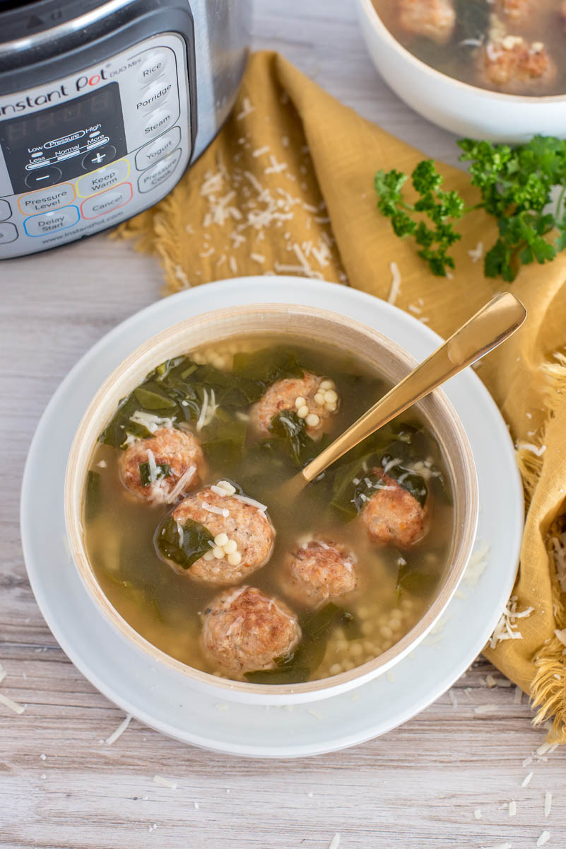 Overhead picture of pressure cooker Italian weeding soup in a white bowl with a spoon, placed on a yellow cloth, in front of an Instant Pot.