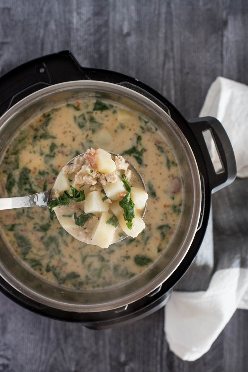 An overhead shot looking into an Instant Pot with the focus on a ladle taking out a heaping spoonful of Zuppa Toscana