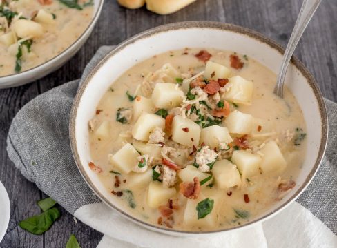 A rustic bowl edged in brown around the rim filled with zuppa toscana and garnished with fresh spinach and bacon