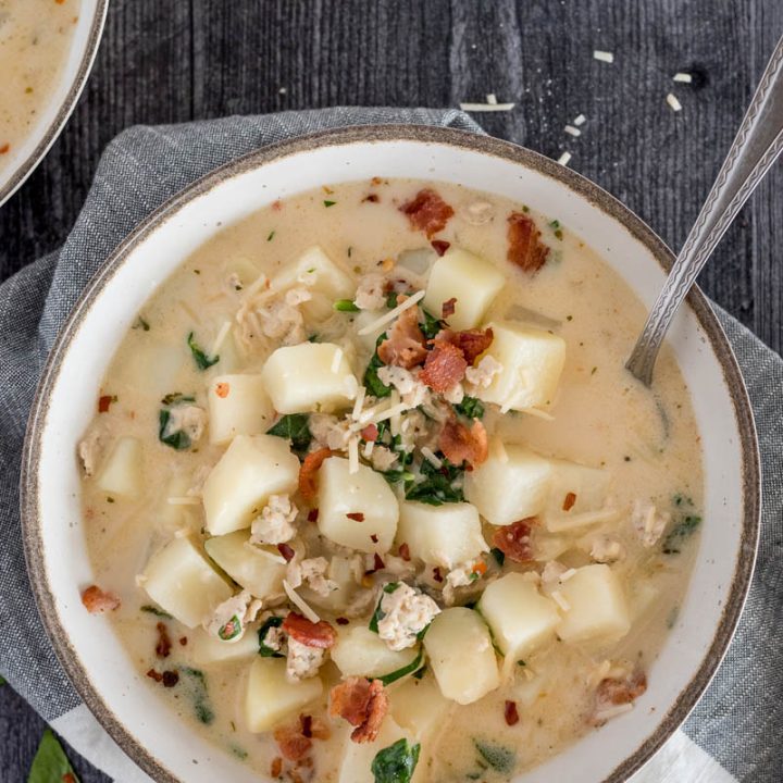 An overhead shot of a bowlful of zuppa toscana sitting on a green and white napkin with breadsticks and extra parmesan for garnish