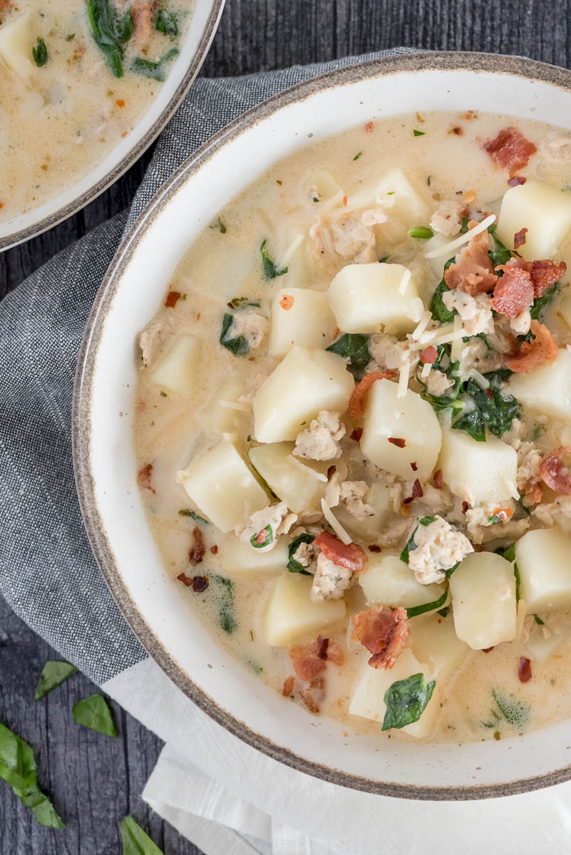 A tight vertical shot of a rustic bowl filled with potatoes, sausage, spinach, and garnished with bacon and parmesan cheese